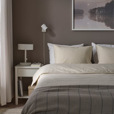 Slaapkamer met RUNDHAGTORN dekbed op groot bed, gestreept beddengoed, lichte kussens, grijze muur, minimalistische foto, nachtkastje met lamp en boeken.