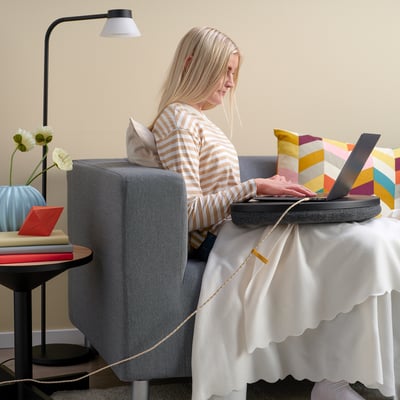 Vrouw in gestreept overhemd werkt op laptop aan tafel met lamp en bloemen.