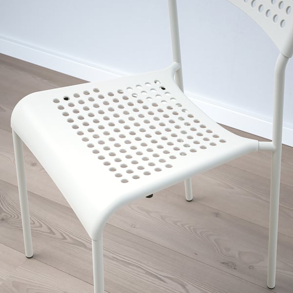 Twee moderne witte stoelen met geperforeerde zittingen, netjes gestapeld op een lichte houten vloer, met een strak design en hoogwaardig vakmanschap.