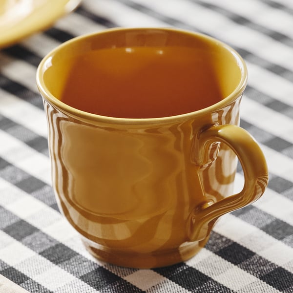 Gouden mok op gestreept tafelkleed, glad oppervlak, robuust design.