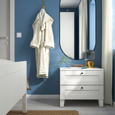 Moderne slaapkamer met blauwe muren; wit SANNIDAL nachtkastje, hangende badjas, grote spiegel en decoratieve stukken.