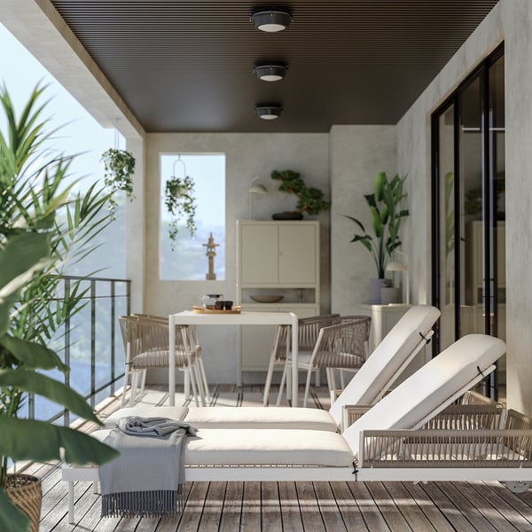 Modern balkon met witte SEGERÖN ligstoelen, houten vloer, glazen balustrade en potplanten.