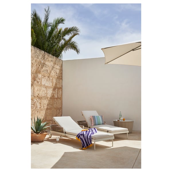 Moderne loungeruimte buiten met witte SEGERÖN-fauteuils, gestreepte handdoek, bijzettafel en palmboom.