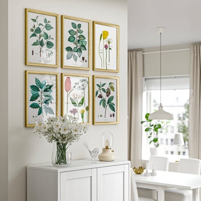 Moderne woonkamer met botanische prints, witte kast, vaas met bloemen en eethoek.