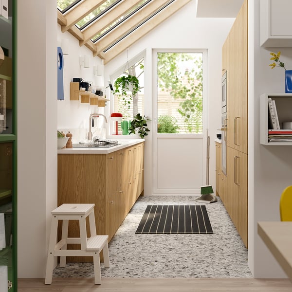 Moderne keuken met SINARP licht eiken kasten, witte werkbladen en een minimalistische inrichting met een klein wit opstapje.
