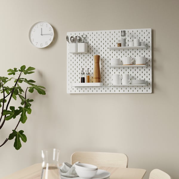 Ophangbord aan de muur SKÅDIS met planken en keukengerei; klok en plant in de buurt.