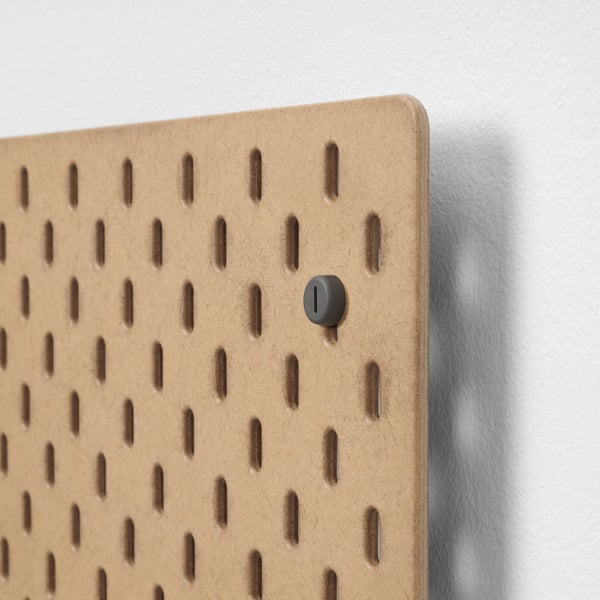 Een close-up van een houten ophangbord met gelijkmatig verdeelde gaten en een zwarte ingestoken knop.