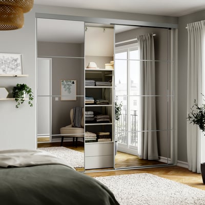 Moderne slaapkamer met gespiegelde kastdeuren, groen hoofdeinde bed en grote ramen met grijze gordijnen.