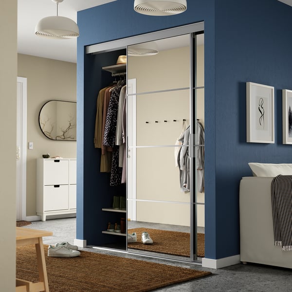 Moderne kamer met SKYTTA spiegelkast, blauwe muren, witte meubels en houten accenten; kasten grote spiegel reflecteert ruimte.
