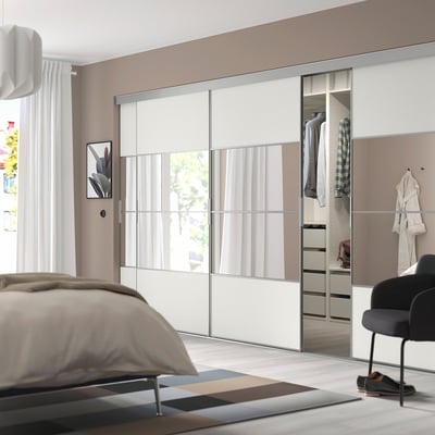 Moderne slaapkamer met glazen schuifdeuren, georganiseerde kleding en zwarte stoel.