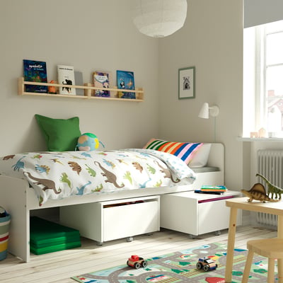 Kinderslaapkamer met SLÄKT-bed, dinosaurusbeddengoed, speelgoedauto, boeken en opbergruimte onder het bed.