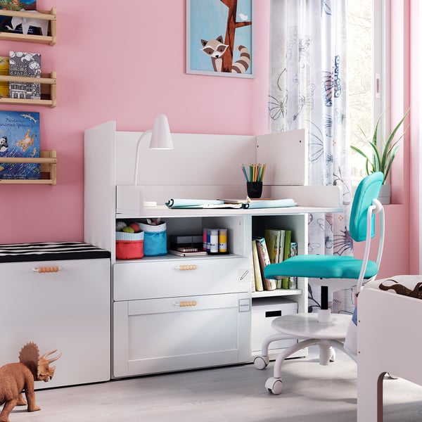Felroze kinderkamer SMÅSTAD wit bureau en ladeset, blauwe stoel, speelgoeddinosaurus en wandplanken met boeken en speelgoed.