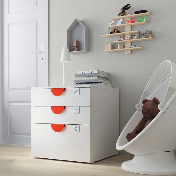 Moderne kinderkamer met een witte SMÅSTAD kist, lichthouten planken en een witte hangstoel met een teddybeer.