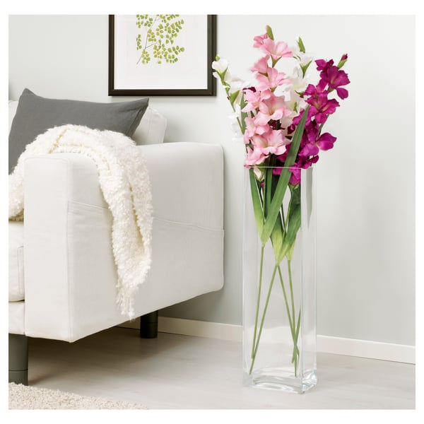 Heldere vaas met roze en paarse bloemen staat naast een witte stoel met een deken.