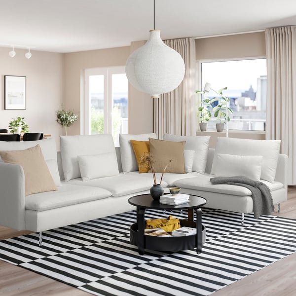 Minimalistische woonkamer met witte SÖDERHAMN sectional, zwarte salontafel, gestreept vloerkleed en groot raam met uitzicht op de stad. Gezellig en modern design.