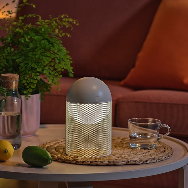 Een moderne lamp op een tafel, met een plant, beker en fruit in de buurt.