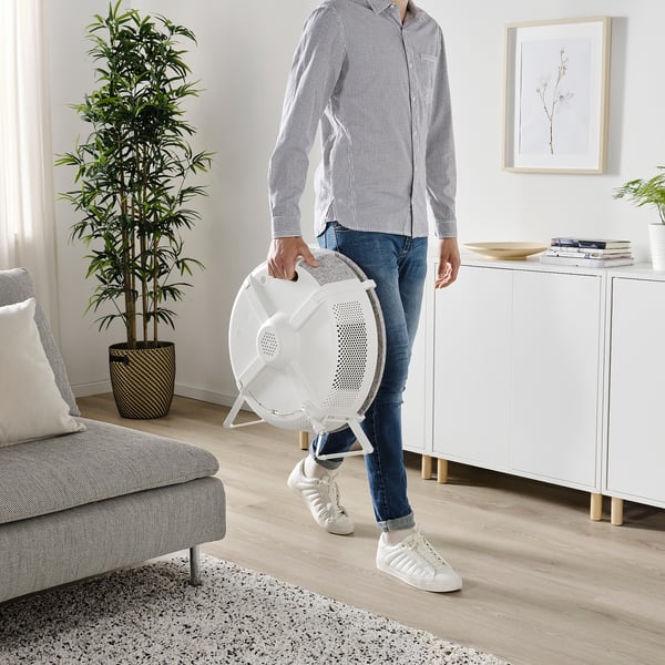 Persoon die een witte STARKVIND-luchtreiniger vasthoudt in een woonkamer, met een draagbaar ontwerp met een geïntegreerd handvat.