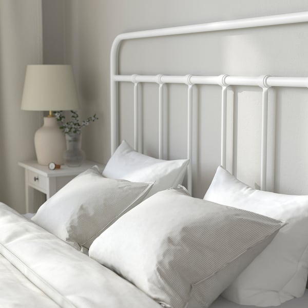 Moderne slaapkamerscène: gezellig wit bed met gestreepte kussens, metalen hoofdeinde, nachtkastje met lamp en bloemen.