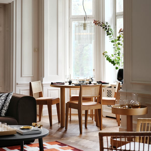 Moderne eetkamer met houten tafel, donkere bank, groot raam en elegante kroonluchter.