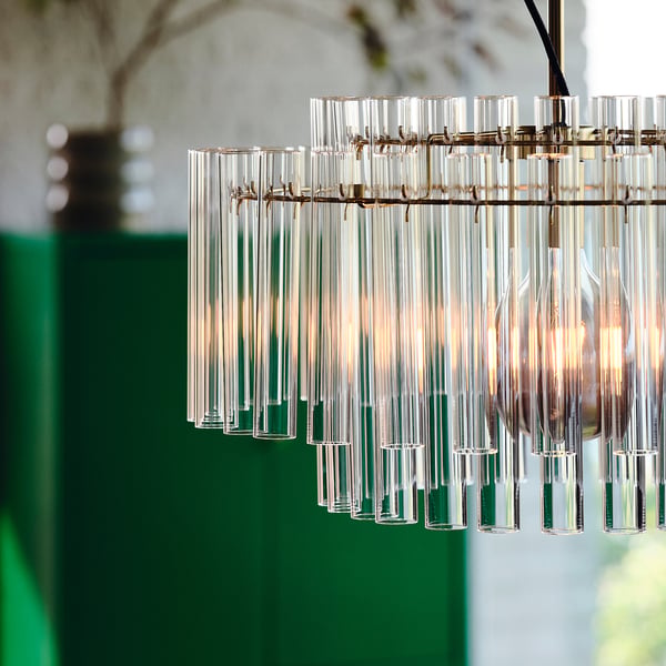 Aan een messing geklede haak hangt een moderne kroonluchter met 54 glazen cilinders. Hij geeft direct licht, geschikt voor een eettafel of woonkamer.