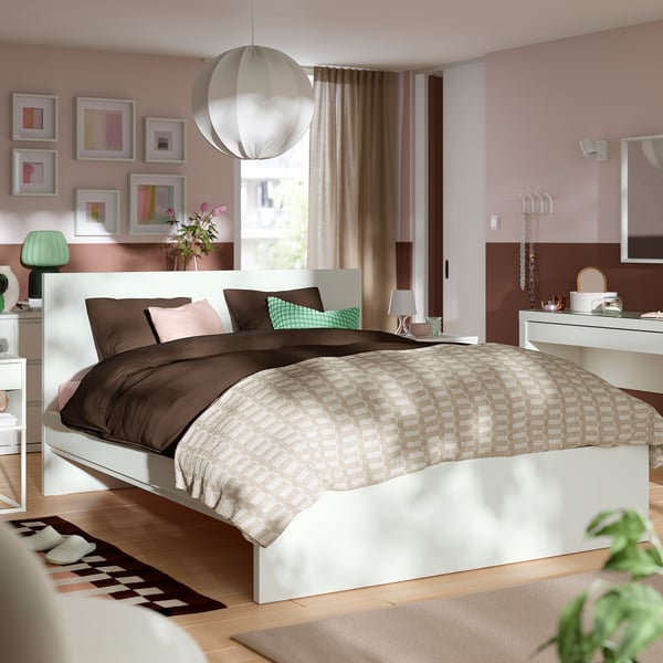 Modern wit STORKLINTA-bed, laag profiel, minimalistisch ontwerp, met bruine/beige textiel in een gezellige kamer.