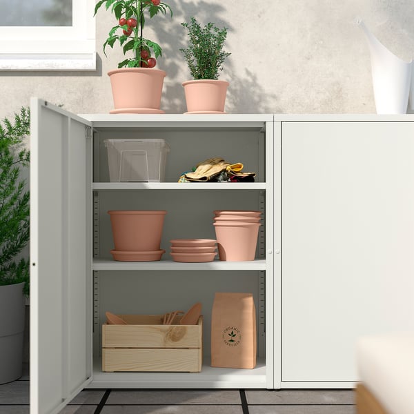 Witte SUNDSÖ kast met verstelbare planken voor oranje terracotta potten en tuingereedschap. Ideaal voor binnen/buiten opslag.