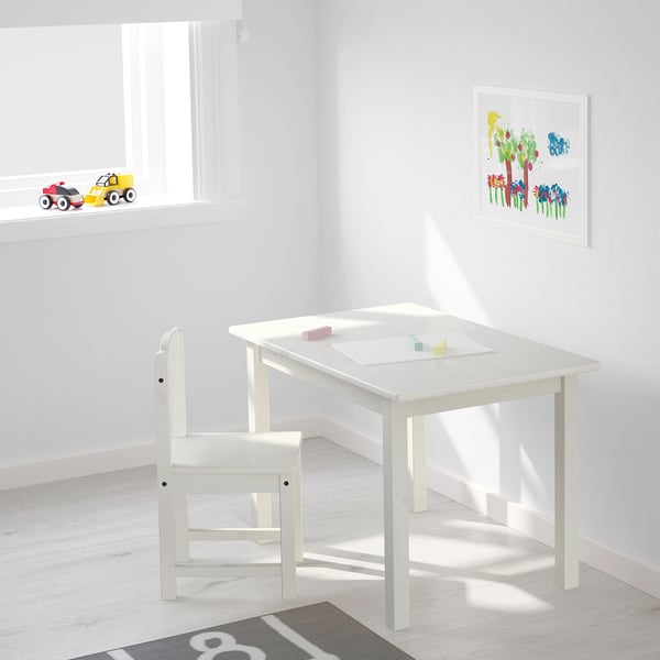 Childs studieruimte met witte tafel en stoel, met kleurrijke speelgoedauto's en kunstprint.