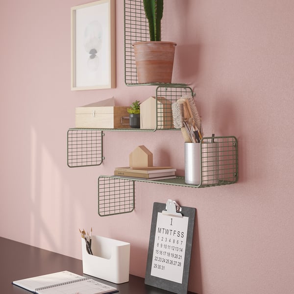 Aan de muur gemonteerde roosterplanken met verschillende items: een potplant, borstels, boeken en een klembord met een kalender. Gepersonaliseerde organisatie op roze muur.
