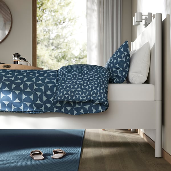Slaapkamer met TONSTAD bed met blauw patroon, groot raam met uitzicht op groen, stoere constructie.