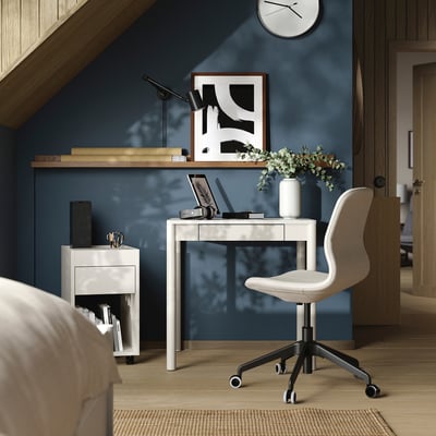 Modern kantoor aan huis met wit TONSTAD bureau, stoel en donkerblauwe muur. Bureau heeft een laptop, bloemen en een klok.