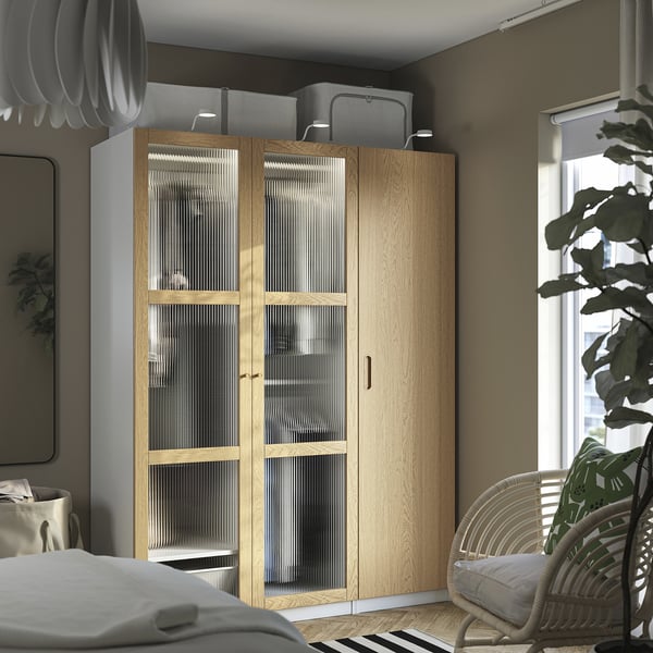 Moderne slaapkamer met TONSTAD glazen deurkast, rieten stoel en groot raam.