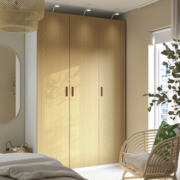 Moderne slaapkamer met TONSTAD kledingkast, rieten stoel, plant en spiegel.