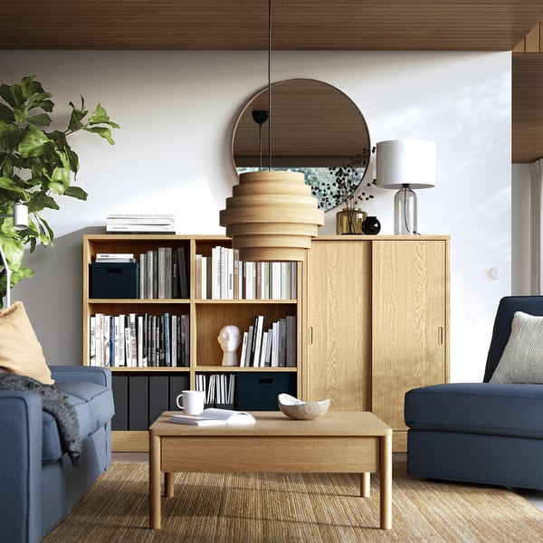 Een moderne woonkamer met een TONSTAD boekenplank, blauwe banken en een groene plant.