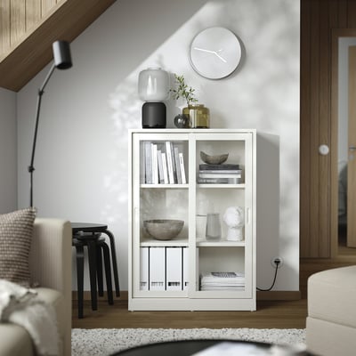 Witte houten boekenkast met glazen schuifdeuren; Houdt boeken, vazen en een klok vast in een moderne woonkamer.