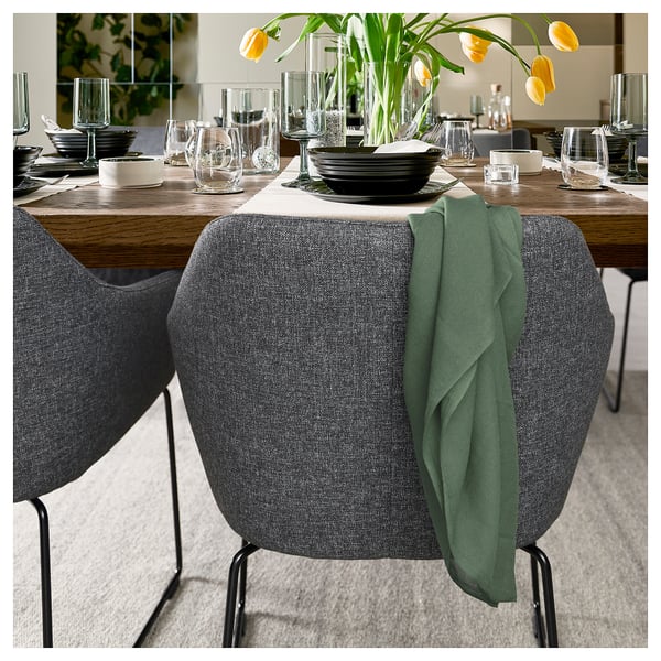 Moderne eetscène met TOSSBERG grijze stoelen, houten tafel, zwarte platen, glaswerk en gele bloemen.