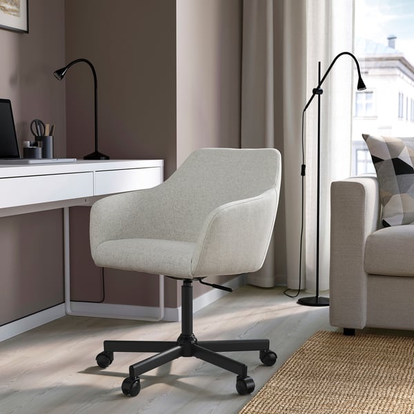 Een moderne, lichtgrijze TOSSBERG bureaustoel met een hoge rugleuning en een zitting met kussens, gepositioneerd naast een wit bureau en een bank in een gezellige kamer.