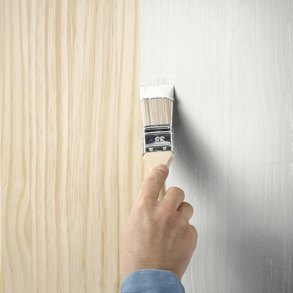 Een hand gebruikt een penseel om een houten oppervlak te schilderen met TRIXIG, een semi-matte meubelverf op waterbasis.