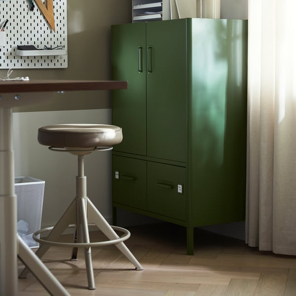 Een moderne groene kantooropstelling omvat een hoge kast, een tafel met een draaistoel en een opbergsysteem voor ophangborden.