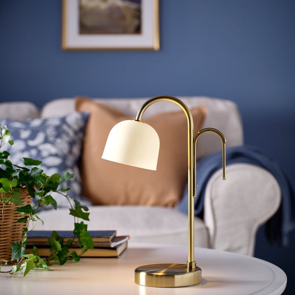 TVÅMASTAD lamp op tafel met bank & plant. Gouden lamp met matglazen kap en draagbaar handvat.