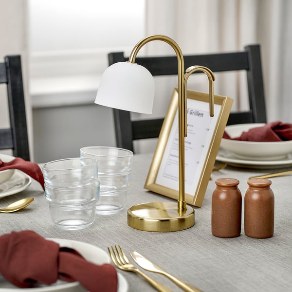 Een stijlvolle, draagbare lamp op een tafel, die oplicht met een warm wit licht, met een koperen voet en matglazen kap.