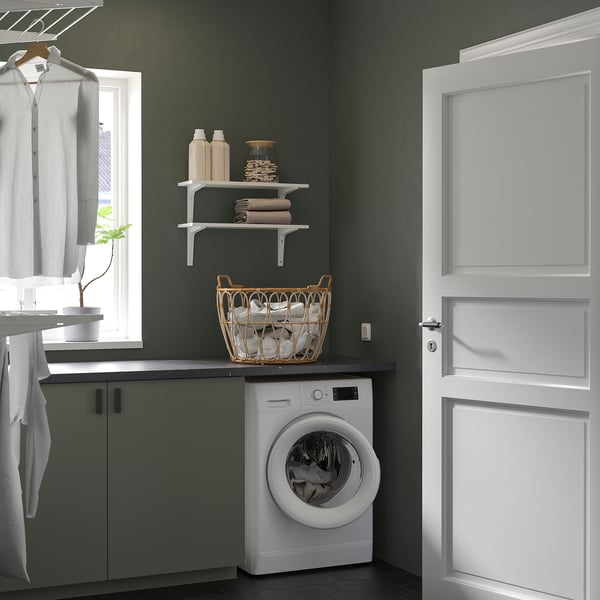 Kleine, witte UDDARP combo wasmachine/droger past netjes onder groene planken, efficiënt voor de was in compacte ruimtes.
