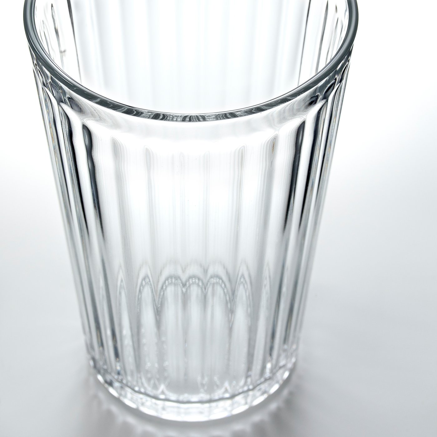 Glazen beker met verticale ribbels, helder en transparant, rustend op een wit oppervlak.