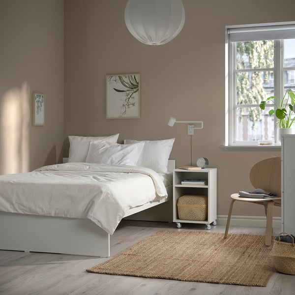 Slaapkamer met modern, wit VIHALS bed gecentreerd tegen bruine muur, aangevuld met eenvoudige houten bijzettafel en trapsgewijze lamp.