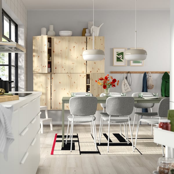 Moderne keuken met grenen kasten, witte stoelen en een levendig vloerkleed.