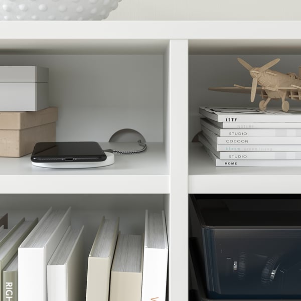 Witte boekenplank met zwarte gadget, boeken en houten vliegtuigmodel.