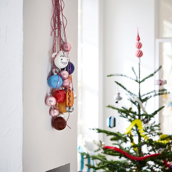 Kleurrijke VINTERFINT-balletjes hangen: rood, blauw, roze, oranje; sommige dierlijk, groter dan een boom.