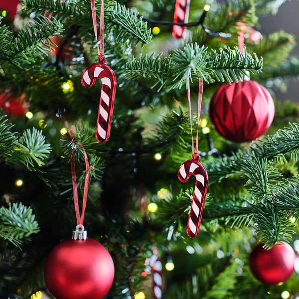 Kerstboom versierd met rode glazen ornamenten en zuurstokken, lampjes fonkelen op de achtergrond.