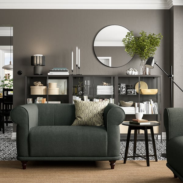 Elegante woonkamer met VISKAFORS groene stoffen fauteuils, vloerkleed met patroon, boekenplank met decor en vloerlamp, het creëren van gezellige en stijlvolle ruimte.