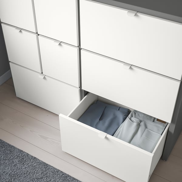 Wit dressoir met gladde lades en verstelbare poten. Een lade open, met kleding.