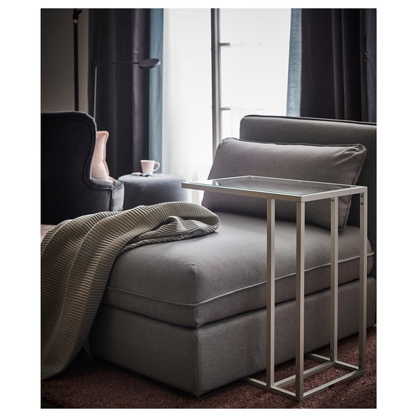 Moderne woonkamer met grijze stoffen fauteuil, kleine tafel met glazen blad en gestreepte deken.
